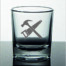 Das "Hammer & Säge" Schnapsglas zeigt ein graues Hammer-und-Säge-Motiv auf klarem Glas, liegend auf spiegelndem Untergrund. Wertica Shop