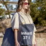 Eine Frau mit Sonnenbrille und beigem Shirt trägt draußen die große graue Einkaufstasche "Big Bag" mit "Inhalt 37 l" vor Bäumen und Gebäuden. Wertica Shop