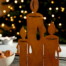 Metall-Engel mit Herz im Rost-Look auf Holzfuß, davor Walnüsse, dahinter ein leuchtender Weihnachtsbaum auf einem Holztisch. Wertica Shop