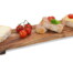 Das Akazien-Servierbrett mit Griffen präsentiert Käse-, Tomaten- und Pastetenbrote sowie Kirschtomaten, stilvoll auf weißem Grund angerichtet. Wertica Shop
